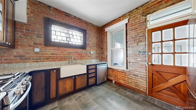 interior space with light stone counters, brick wall, dark brown cabinetry, stainless steel appliances, and sink