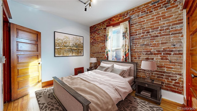 bedroom featuring light hardwood / wood-style flooring and brick wall