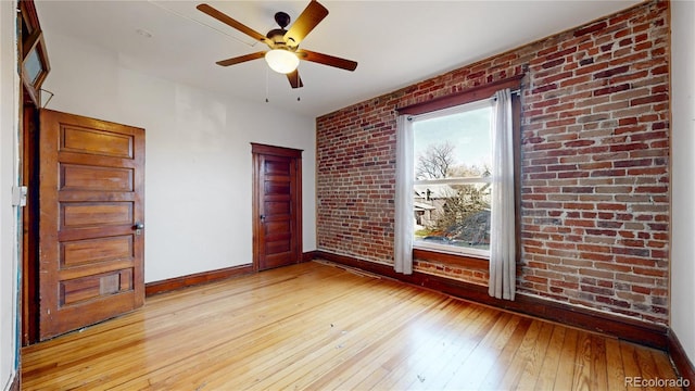 spare room with light wood-type flooring, ceiling fan, and brick wall