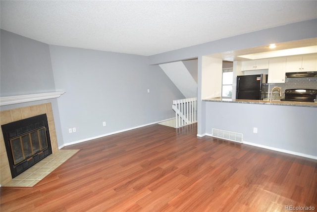 unfurnished living room with a textured ceiling, a tile fireplace, and light hardwood / wood-style flooring