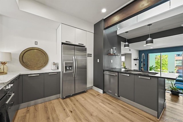 2565 Champa St, Denver, CO 80205 - kitchen featuring appliances with stainless steel finishes, a peninsula, light wood-type flooring, hanging light fixtures, and dark stone countertops