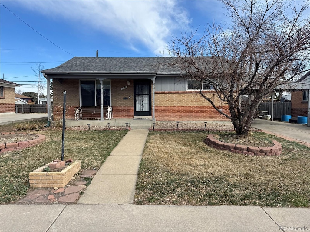 view of front facade featuring brick siding, a shingled roof, fence, a front yard, and covered porch