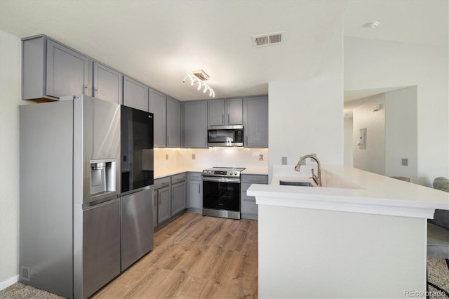 kitchen featuring appliances with stainless steel finishes, sink, gray cabinetry, kitchen peninsula, and light hardwood / wood-style flooring