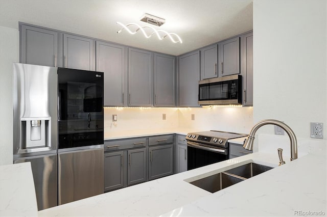 kitchen featuring stainless steel appliances, gray cabinets, light stone countertops, and sink