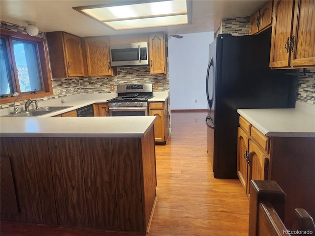 kitchen featuring backsplash, a sink, black appliances, a peninsula, and light wood-style flooring