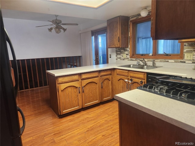 kitchen with freestanding refrigerator, a peninsula, a sink, and light wood-style floors