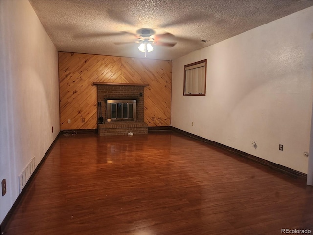 unfurnished living room with ceiling fan, visible vents, wood finished floors, baseboards, and wooden walls