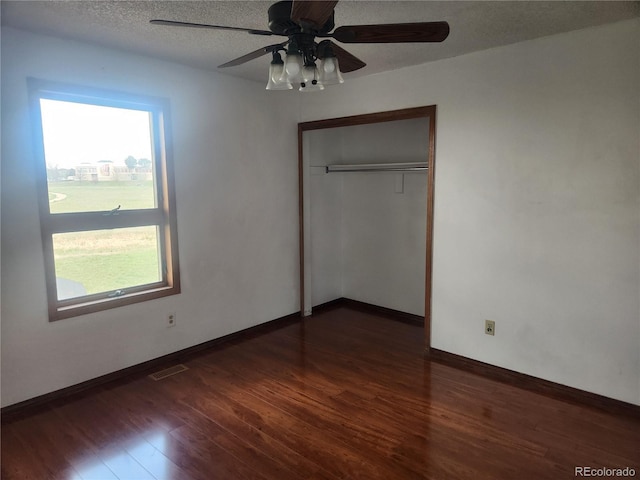 unfurnished bedroom featuring a ceiling fan, visible vents, wood finished floors, baseboards, and a closet