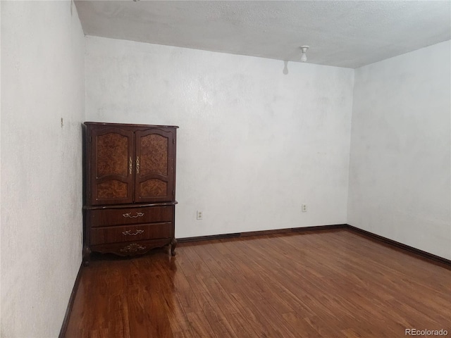 spare room featuring baseboards and dark wood-style floors