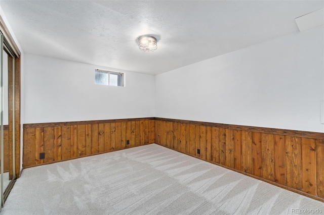 empty room featuring wood walls, light carpet, and a textured ceiling