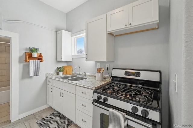 kitchen with sink, light tile patterned floors, stainless steel range with gas stovetop, light stone countertops, and white cabinets