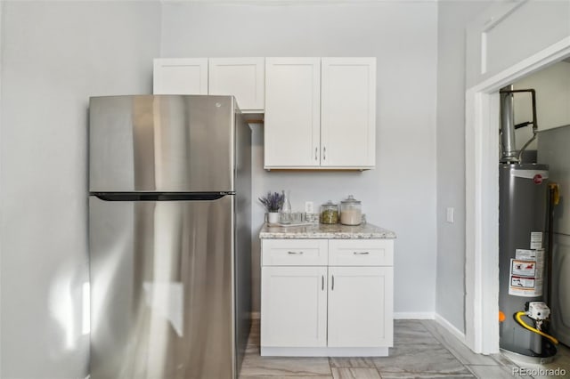 kitchen with white cabinetry, light stone counters, stainless steel fridge, and water heater