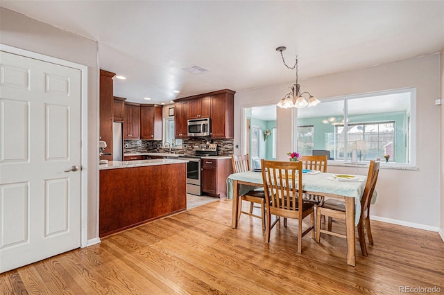 kitchen with a chandelier, light wood-type flooring, appliances with stainless steel finishes, pendant lighting, and backsplash