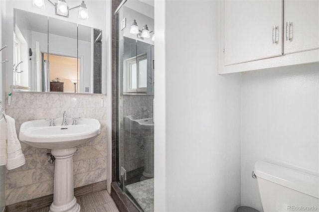 bathroom featuring walk in shower, toilet, sink, and tile walls