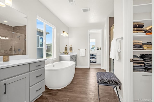 174 Rockingham Cir, Castle Pines, CO 80108 - bathroom featuring a stall shower, wood finished floors, two vanities, a freestanding tub, and a walk in closet
