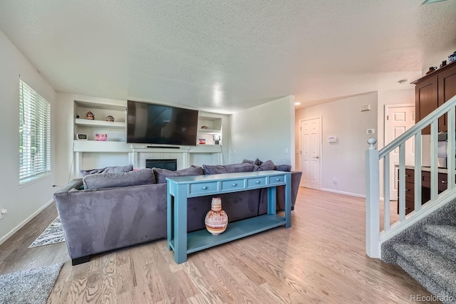 living room with a tiled fireplace, built in shelves, light hardwood / wood-style floors, and a textured ceiling