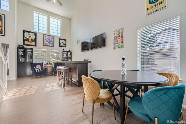 dining space with a high ceiling, light wood-type flooring, and ceiling fan