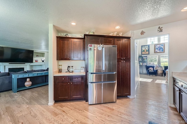 kitchen featuring dark brown cabinets, stainless steel fridge, light hardwood / wood-style floors, and a textured ceiling