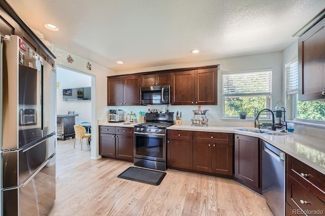 kitchen with sink, light hardwood / wood-style floors, a textured ceiling, dark brown cabinets, and appliances with stainless steel finishes