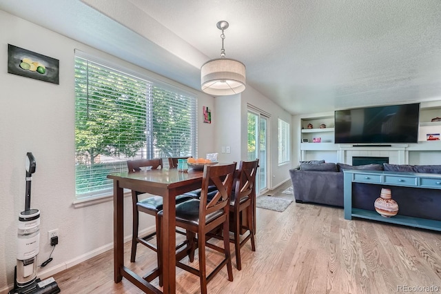 dining room featuring light hardwood / wood-style floors, built in features, a textured ceiling, and a tiled fireplace