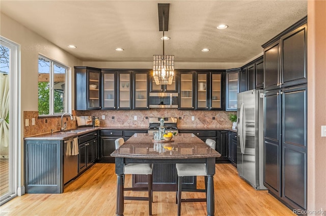 kitchen featuring appliances with stainless steel finishes, a sink, light wood finished floors, a center island, and recessed lighting