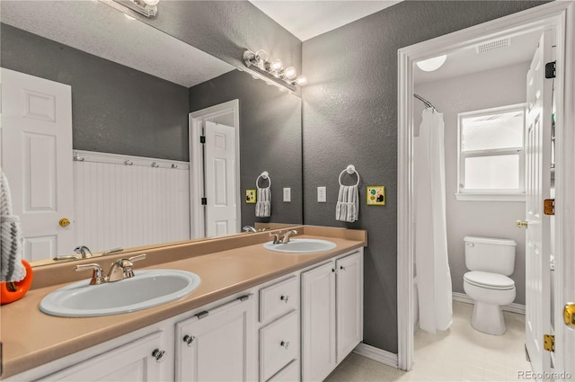 bathroom featuring toilet, double vanity, baseboards, and a textured wall