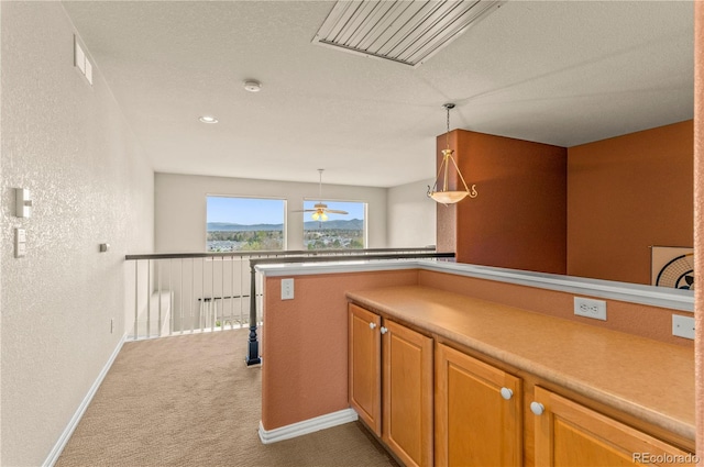kitchen with a textured wall, carpet, baseboards, a ceiling fan, and light countertops