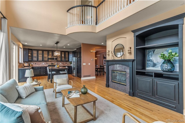 living room with a high ceiling, light wood finished floors, a tiled fireplace, baseboards, and recessed lighting