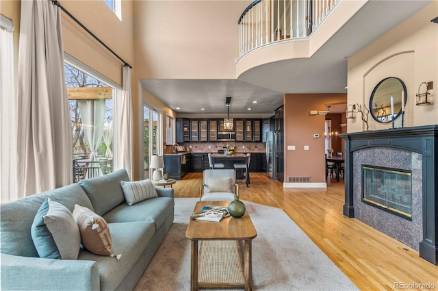 living area featuring a high ceiling, healthy amount of natural light, light wood-type flooring, a glass covered fireplace, and recessed lighting