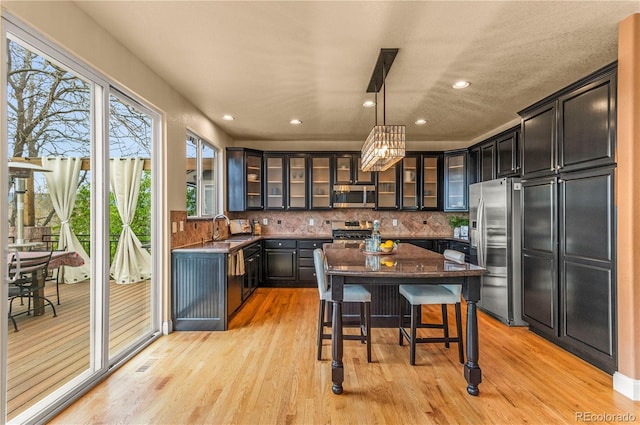 kitchen with stainless steel appliances, a sink, a breakfast bar, decorative backsplash, and glass insert cabinets
