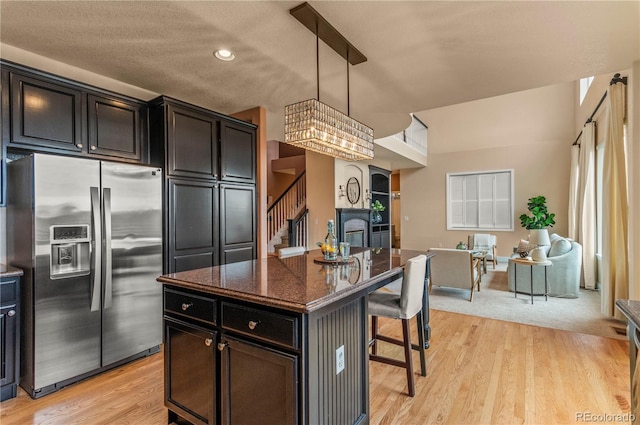 kitchen featuring stainless steel refrigerator with ice dispenser, a kitchen bar, dark stone countertops, a center island, and light wood-style floors