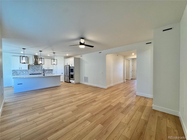 unfurnished living room with a sink, visible vents, baseboards, a ceiling fan, and light wood finished floors