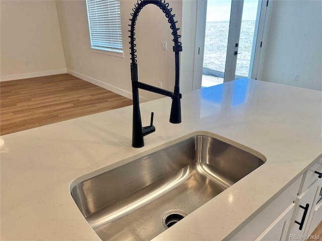 interior details with baseboards, light stone countertops, light wood-type flooring, white cabinetry, and a sink