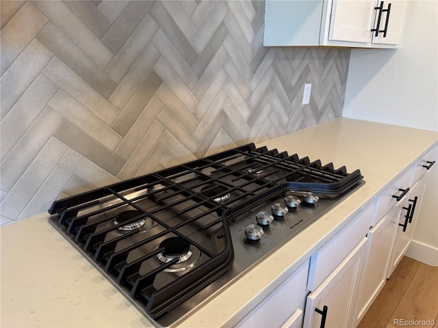 details featuring light wood-style floors, white cabinetry, stainless steel gas cooktop, and backsplash