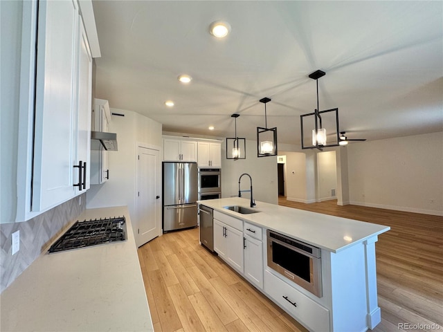 kitchen with appliances with stainless steel finishes, light wood-style floors, white cabinets, and a sink