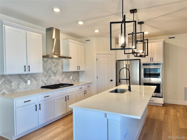 kitchen with stainless steel appliances, light countertops, decorative backsplash, white cabinetry, and wall chimney range hood