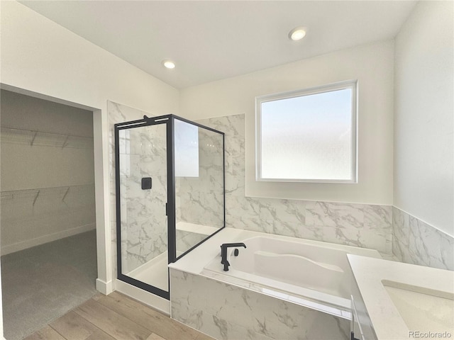 full bath with recessed lighting, wood finished floors, a marble finish shower, a bath, and a walk in closet