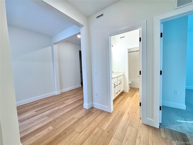 hall featuring light wood finished floors, visible vents, and baseboards