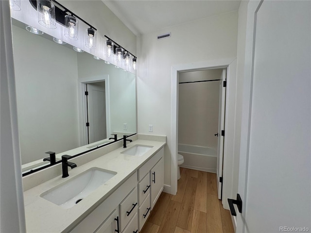 full bathroom featuring toilet, double vanity, a sink, and wood finished floors