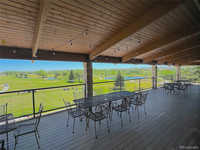 wooden terrace with outdoor dining area, a water view, and a yard