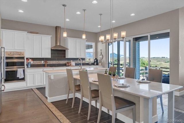 19409 W 88th Dr, Arvada, CO 80007 - kitchen with wall chimney exhaust hood, double oven, dark wood finished floors, an island with sink, and decorative backsplash