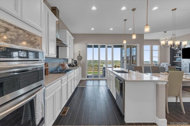 19409 W 88th Dr, Arvada, CO 80007 - kitchen with stainless steel appliances, white cabinetry, wood tiled floors, light countertops, and a center island with sink