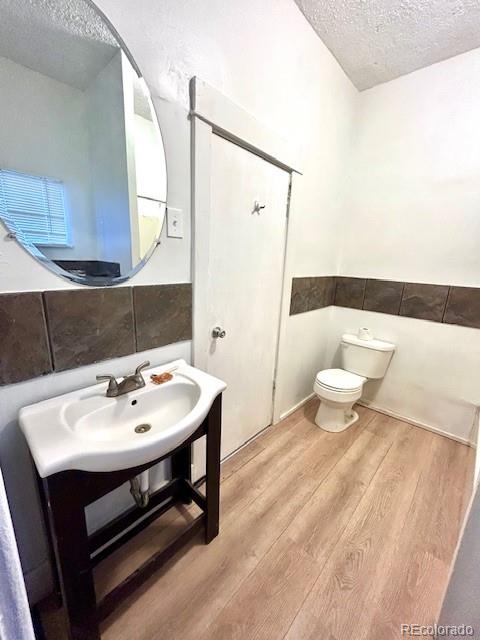 bathroom with a textured ceiling, sink, wood-type flooring, tile walls, and toilet