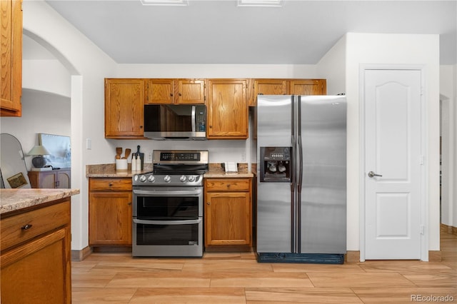 kitchen featuring appliances with stainless steel finishes, brown cabinetry, wood tiled floors, and light stone countertops