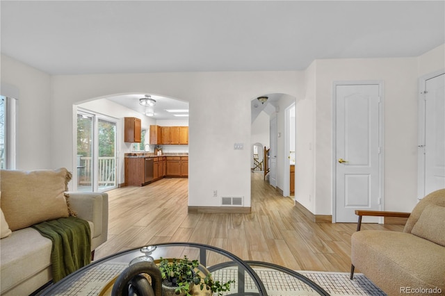 living area with arched walkways, light wood-type flooring, and baseboards