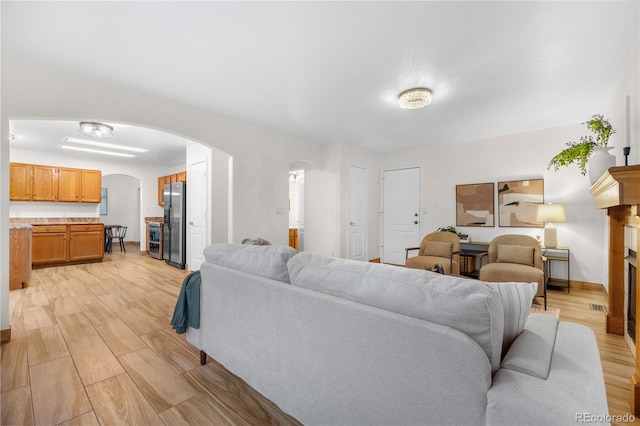 living room with arched walkways, light wood-style flooring, baseboards, and a fireplace