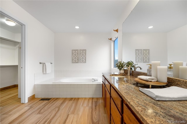 full bath featuring wood finished floors, a garden tub, vanity, and recessed lighting