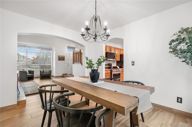 dining area with a chandelier, arched walkways, light wood-style floors, and baseboards