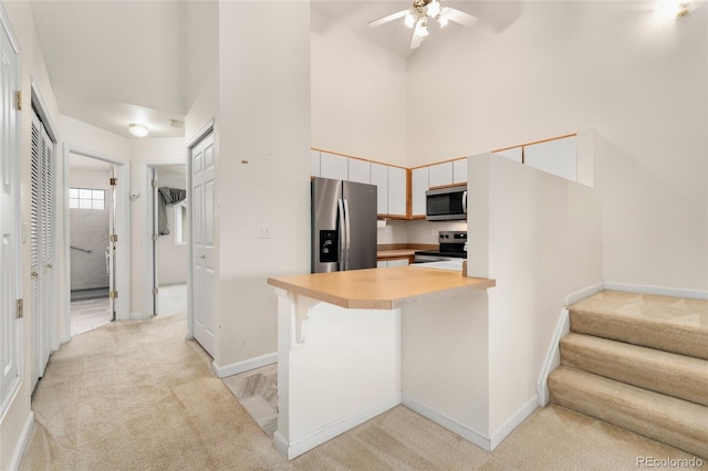 kitchen featuring a breakfast bar, light carpet, a high ceiling, kitchen peninsula, and stainless steel appliances