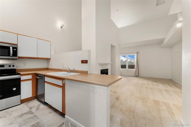 kitchen with white cabinets, sink, appliances with stainless steel finishes, light colored carpet, and kitchen peninsula